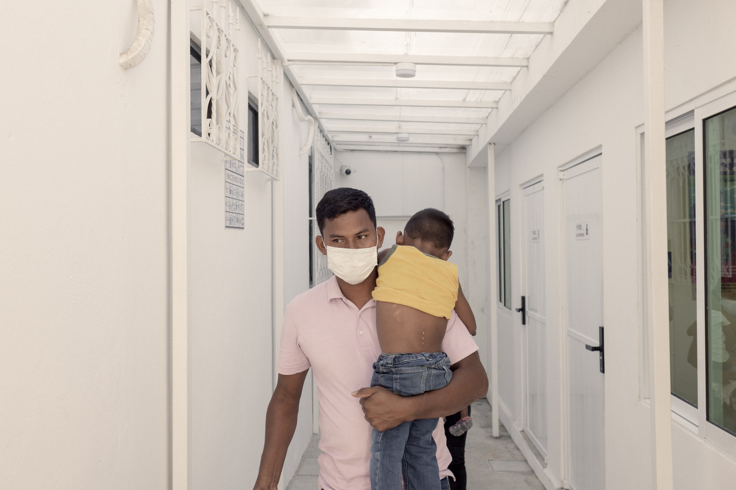 Un hombre con mascarilla camina por un pasillo con un niño en brazos.