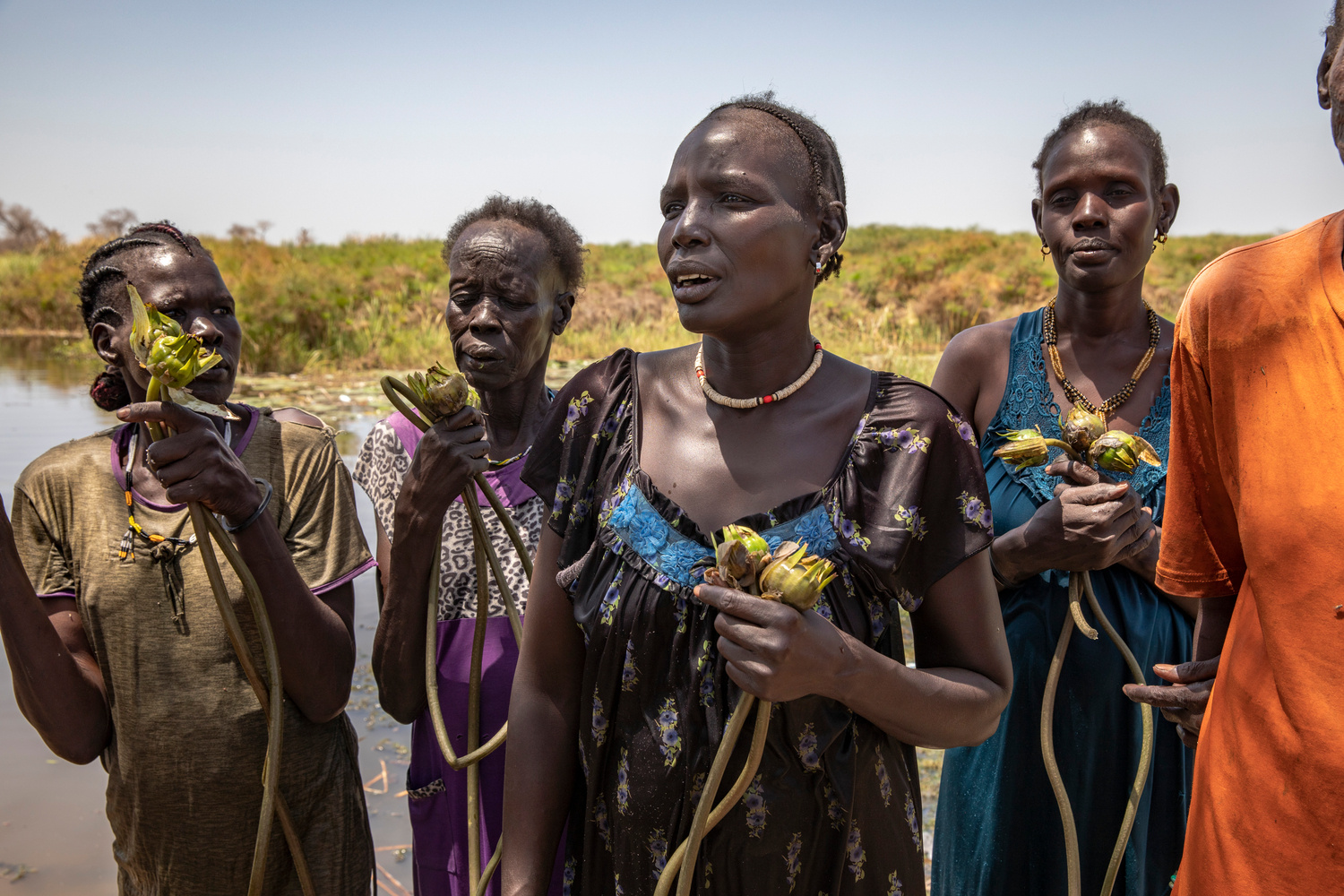 Cuatro mujeres sostienen nenúfares junto al agua.