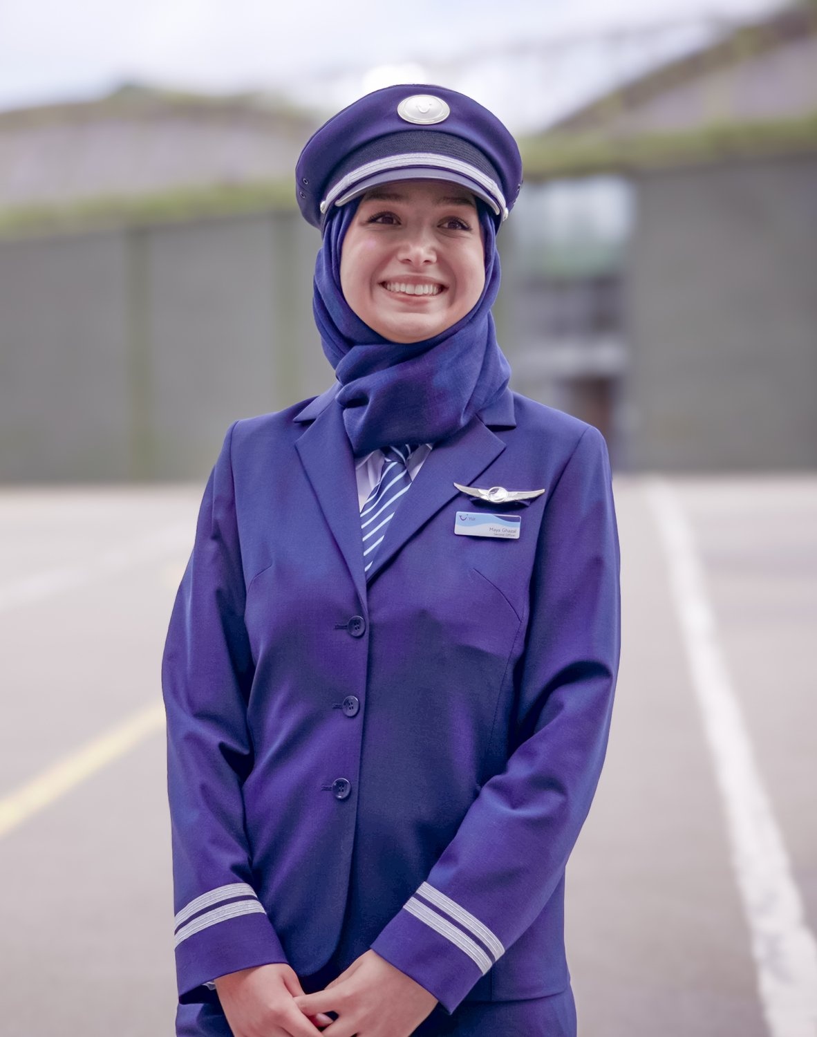 Una mujer con uniforme de piloto morado posa frente al hangar de un avión