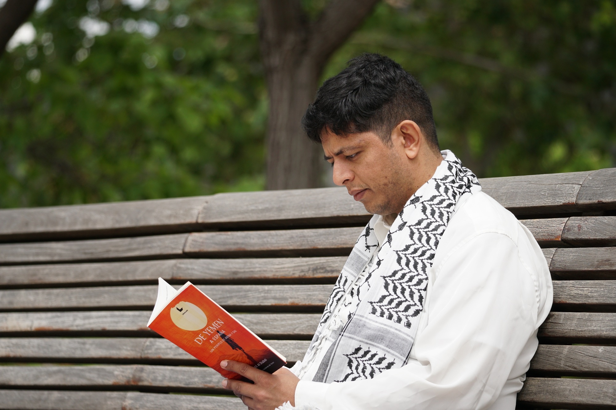 Yousef leyendo el libro De Yemen a Espa&ntilde;a, en un banco de un parque.