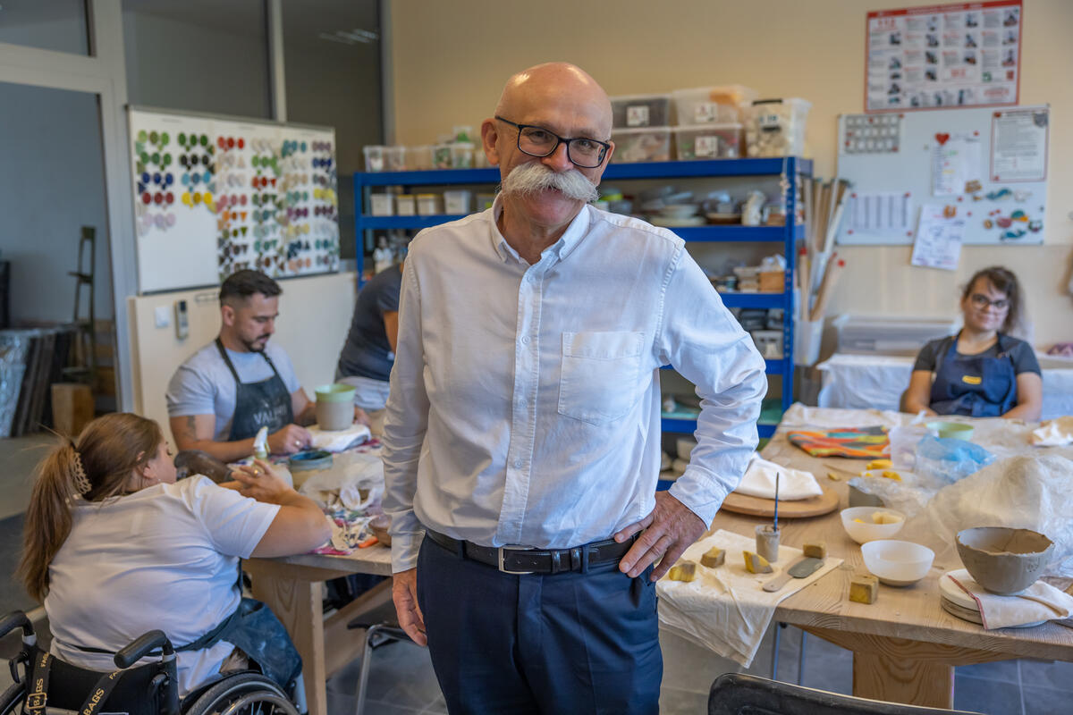 Un hombre que usa un gran bigote blanco posa en un taller de cerámica.