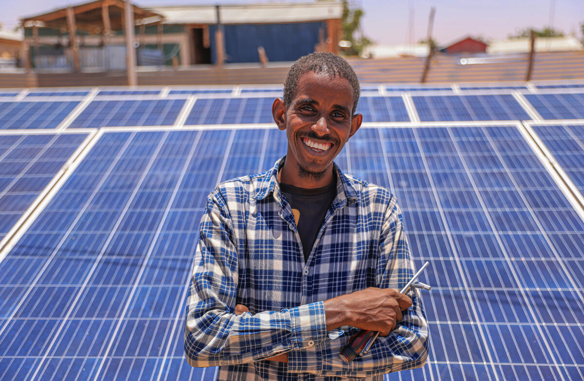 Un hombre somalí sonríe a la cámara; detrás suyo se ven paneles solares.