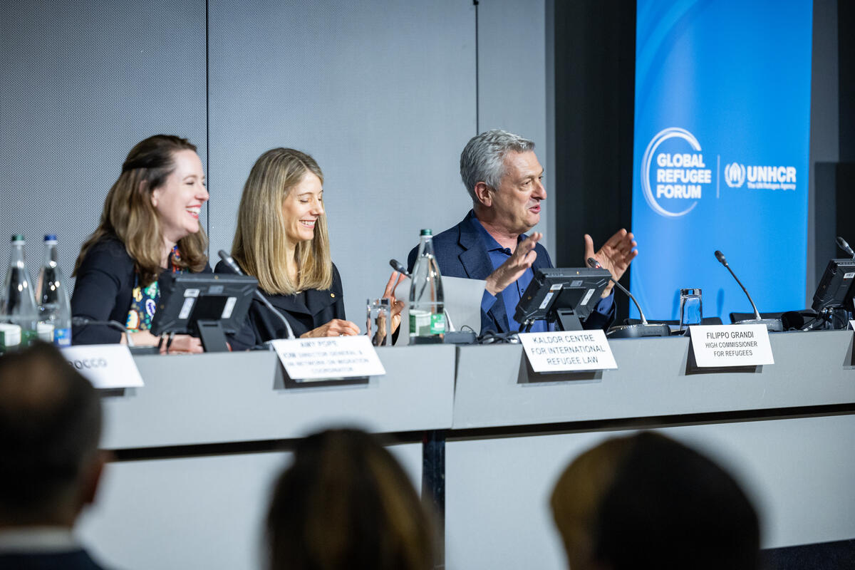 Dos mujeres de cabello rubio, y un hombre de cabello blanco, sentados en un panel.