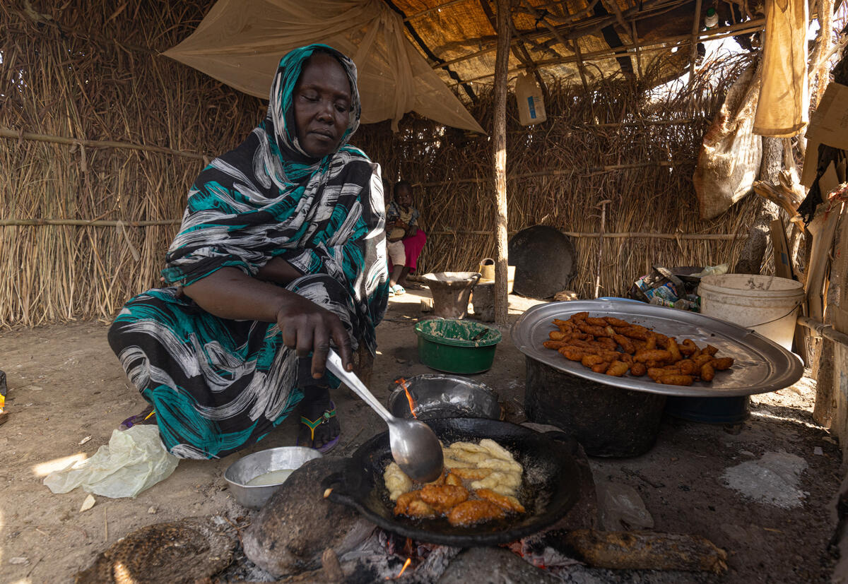 Una mujer sentada en la tierra de su alojamiento cocina en una estufa tradicional