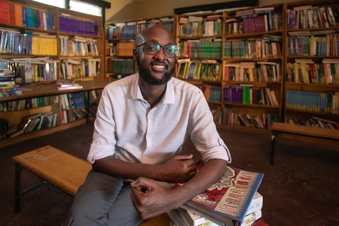 Un hombre somalí que usa anteojos sonríe a la cámara, sentado en una biblioteca