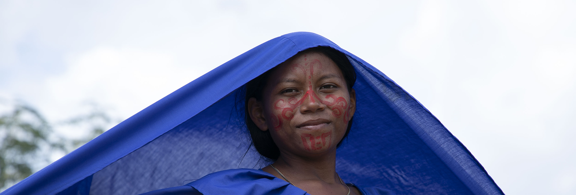 Una mujer indígena vestida de azul mantiene un velo azul sobre su cabeza.