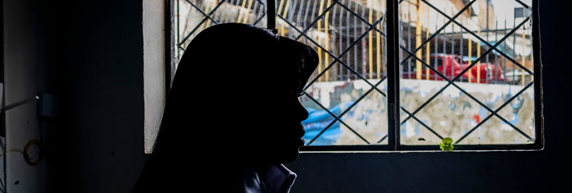 Una mujer fotografiada de perfil y contraluz mira a través de una ventana.