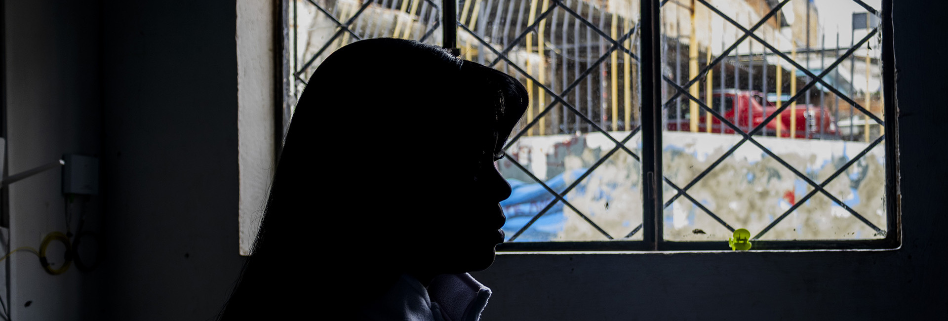 Una mujer fotografiada de perfil y contraluz mira a través de una ventana.