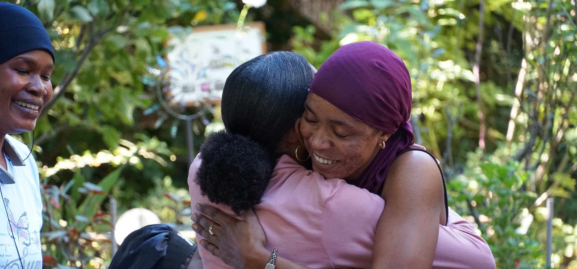Dos mujeres se abrazan en jardín botánico.