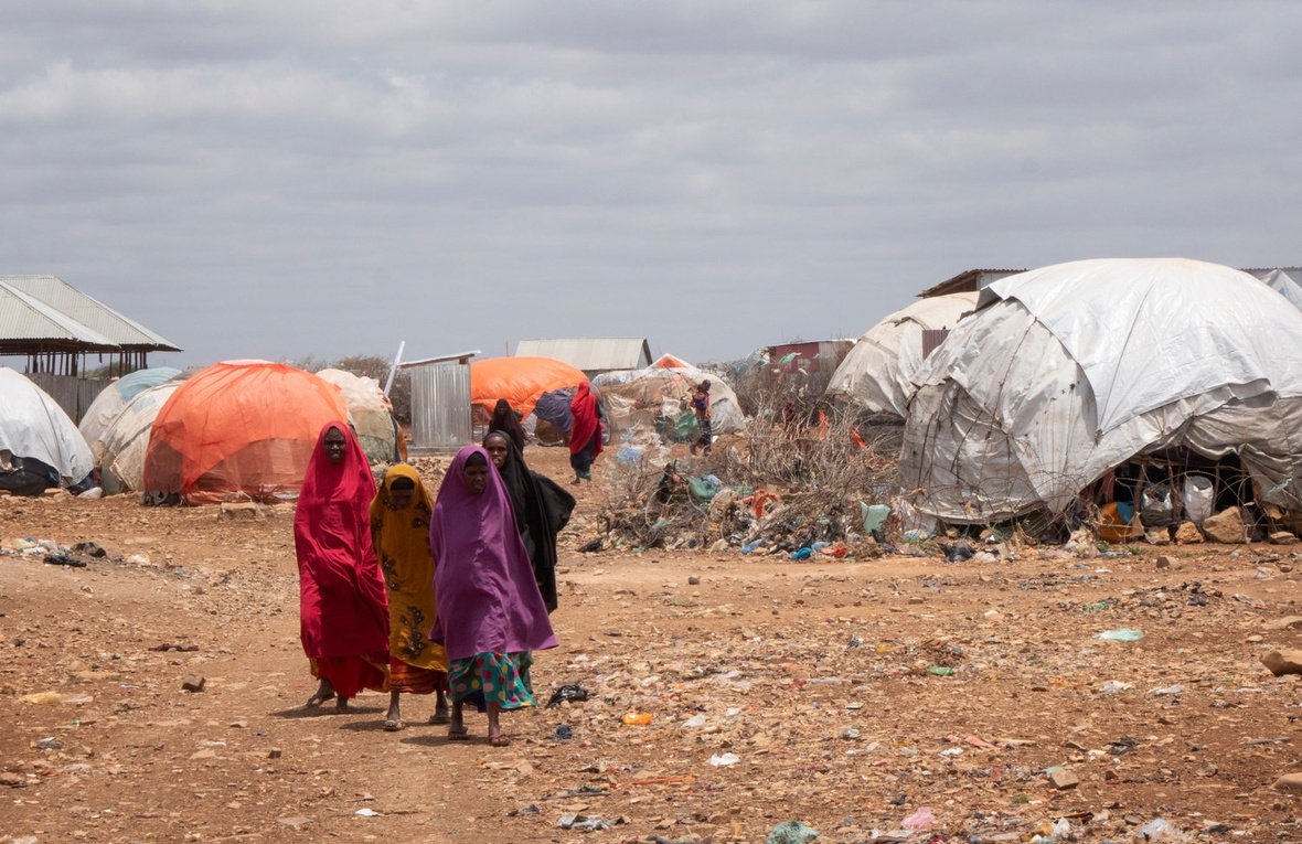 Cuatro mujeres caminan a través de un campamento compuesto por refugios improvisados.