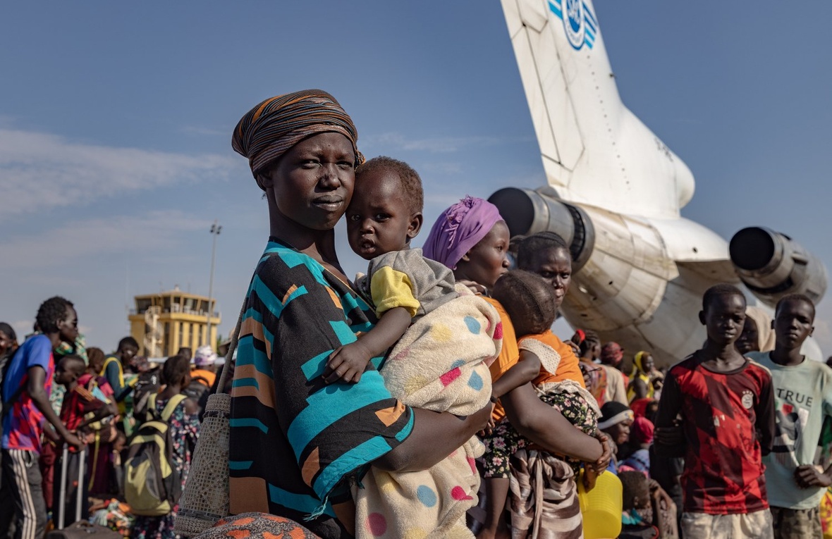Achol Deng y su hija esperan junto a cientos de personas refugiadas sursudanesas que regresan al aeropuerto de Palouch, en el estado sursudanés del Alto Nilo, después de huir del conflicto en Sudán.