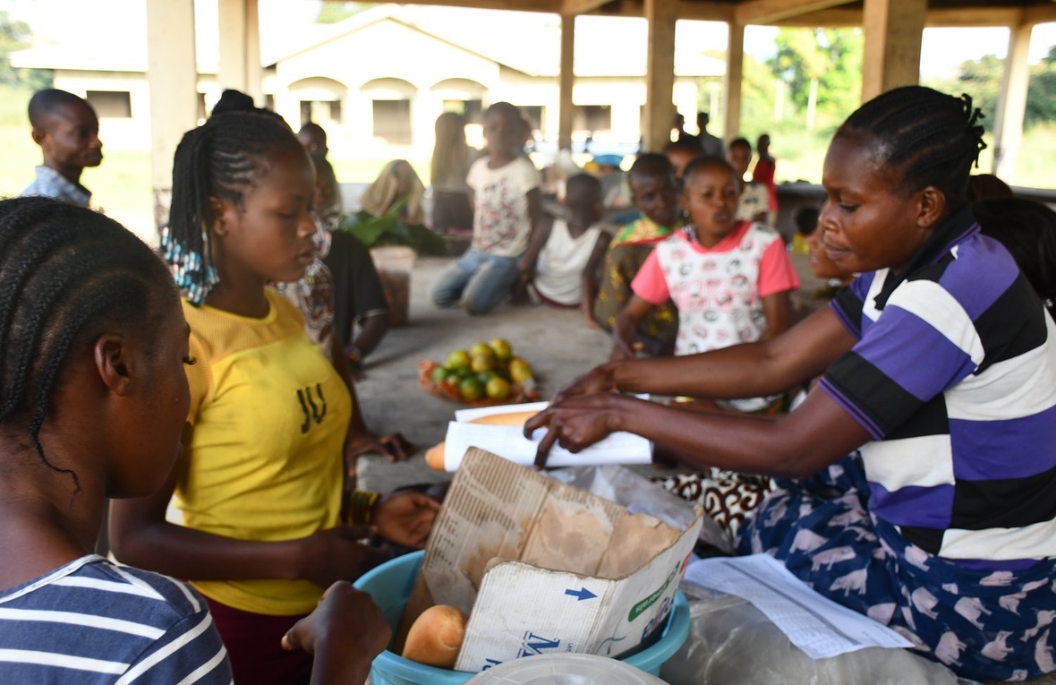 Una mujer en un mercado en República del Congo le entrega a su clienta una hogaza de pan envuelta en papel