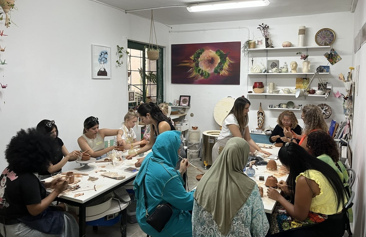 Un aula de clases de cerámica con un grupo de mujeres sentadas modelando arcilla.