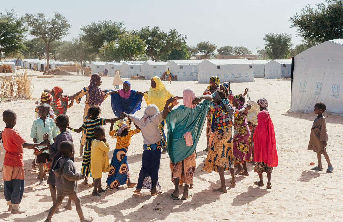 Un grupo de mujeres y niños refugiados juegan al corro en un campamento.