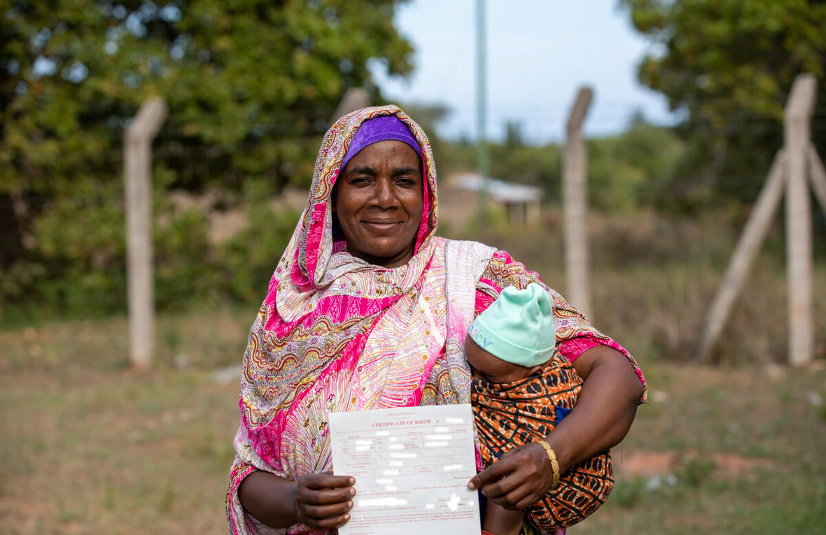 Una mujer Pemba de Kenia sonríe mientras sostiene a su bebé en brazos. Muestra orgullosa un documento