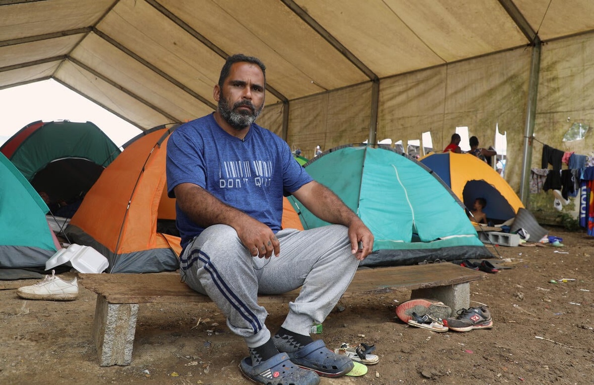 Un hombre sentado en un banco entre pequeñas carpas de acampar.