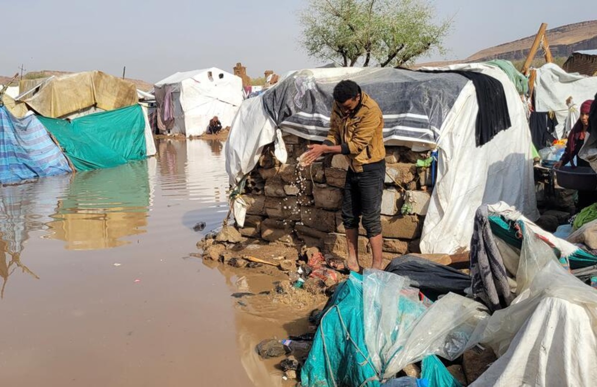 Una personas sacando agua de un alojamiento temporal en medio de un asentamiento inundado.
