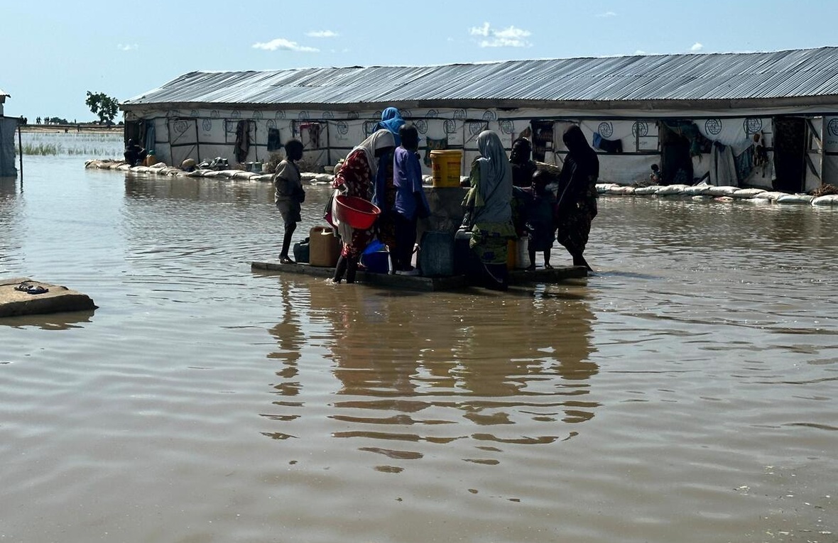 Un grupo de personas intentan acceder a una fuente de agua potable, en medio de un paisaje inundado.