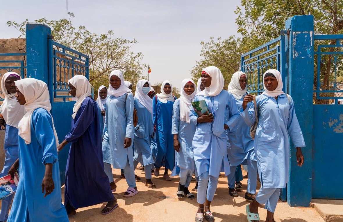 Un grupo de jovencitas sudanesas atraviesa una reja color azul; cada una de ellas lleva la cabeza cubierta con un manto color blanco y porta un atuendo azul claro.