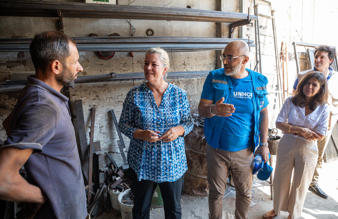 Dos mujeres y dos hombres de pie conversando. Un hombre viste playera y chaleco de ACNUR azul
