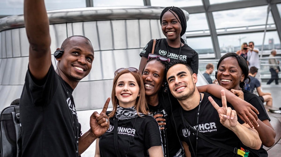 Un grupo de personas jóvenes, que llevan playeras de ACNUR, se toman una selfi.
