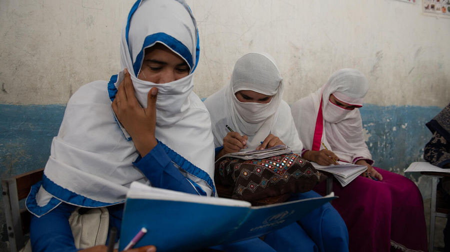 Tres estudiantes afganas que llevan un hijab están sentadas en un aula escribiendo en sus cuadernos.
