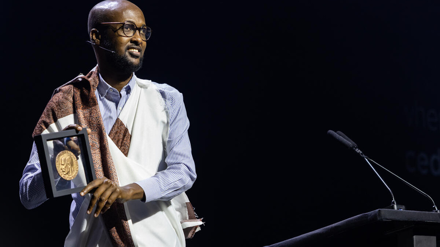 Un hombre somalí, que usa anteojos y viste un traje tradicional, sonríe mostrando la medalla que recibió por haber sido electo ganador global del Premio Nansen