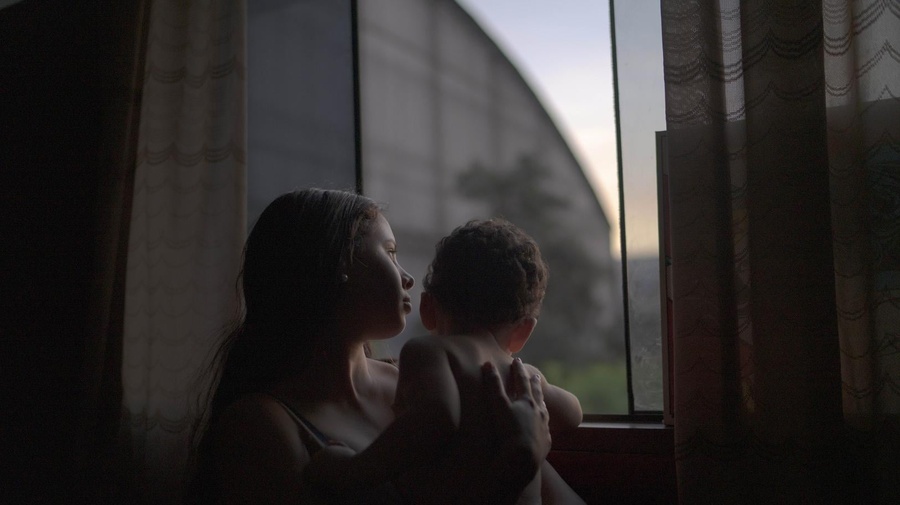 Yenifer está de pie con su hijo de 1 año junto a la ventana de la habitación en la que vive con su pareja a una hora de Lima, Perú. Llegaron a Perú en noviembre de 2019 desde Valencia, Venezuela.