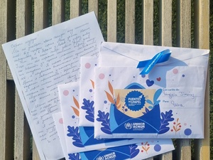 Una carta escrita a mano con tinta negra en una hoja de papel blanco, y sobre de esta, tres sobres con decoraciones azules
