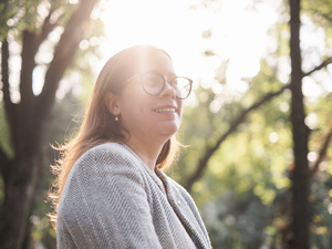 La luz del sol brilla a través de los árboles sobre una mujer que lleva lentes y un blazer gris