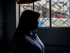 Una mujer fotografiada de perfil y contraluz mira a través de una ventana.