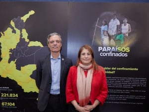 Un hombre y una mujer posan para la cámara delante de un cartel con el mapa de Colombia y el afice de la exposición Paraísos Confinados.