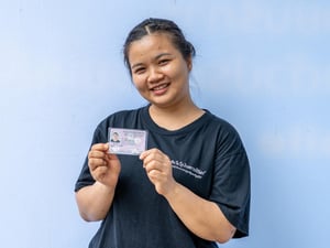 Una joven sonriente que viste una camiseta negra sostiene con sus dos manos un documento de identidad