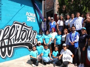 Jóvenes posan por una foto de grupo al lado de un mural.
