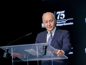 Un hombre vestido con traje pronuncia un discurso de pie ante un atril transparente, con un fondo oscuro.