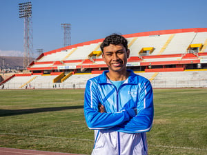 Un joven con uniforme deportivo azul claro con blanco, posa cruzado de brazos de pie en una pista de atletismo