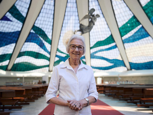 Una mujer de cabello blanco con lentes y camisa blanca en el interior de una gran iglesia con cúpula de cristal