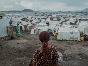 Una mujer de espaldas, de pie sobre el lodo, frente a cientos de tiendas que se extienden hasta el horizonte.
