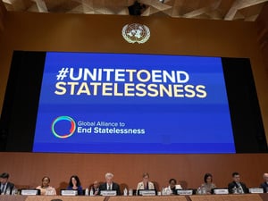 En una gran pantalla, por encima de un panel de personas sentadas, se lee en inglés UNIDOS PARA PONER FIN A LA APATRIDIA. Después: Alianza Global para poner fin a la apatridia
