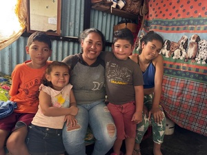 Una mujer sentada sobre una cama con sus cuatro hijos (dos niñas y dos niños). La familia sonríe a la cámara.