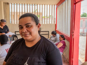 Una mujer posa para la cámara en un salón donde se encuentran varias personas realizando trámites.