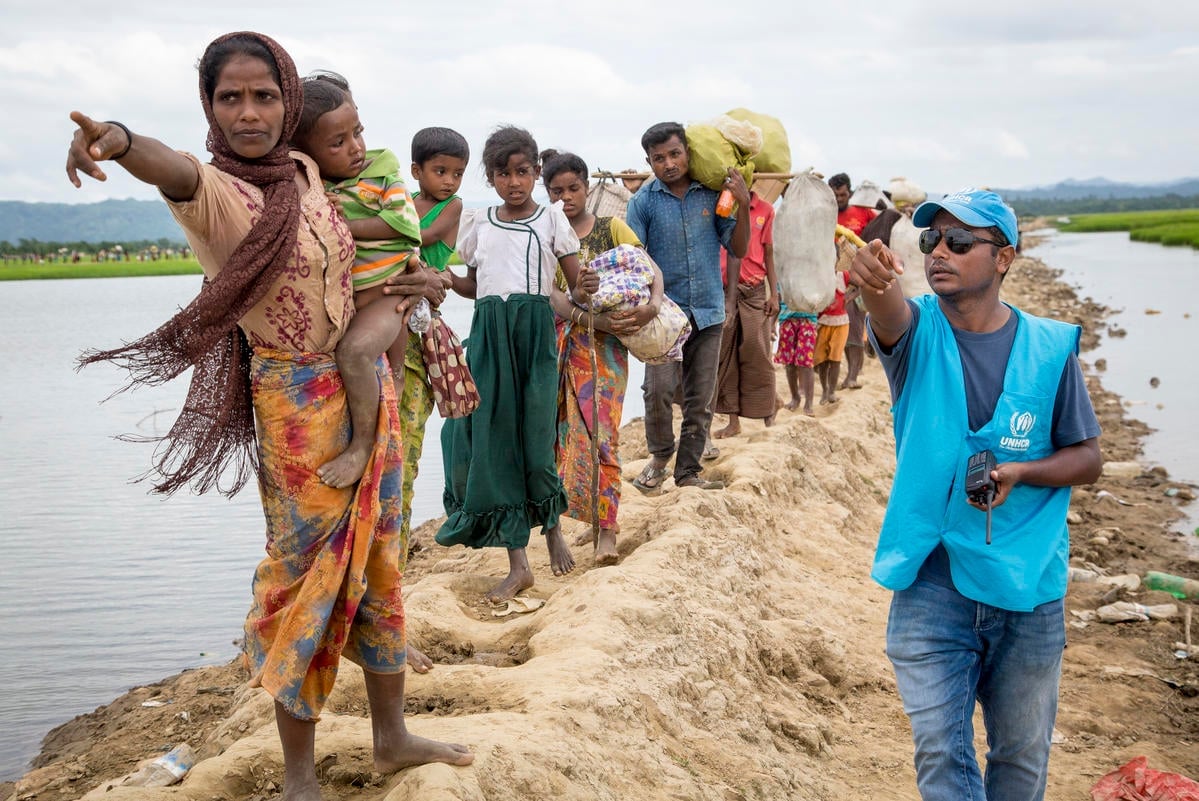 Una trabajadora de ACNUR le indica a un grupo de personas rohingyas refugiadas dónde se encuentra el centro de tránsito.