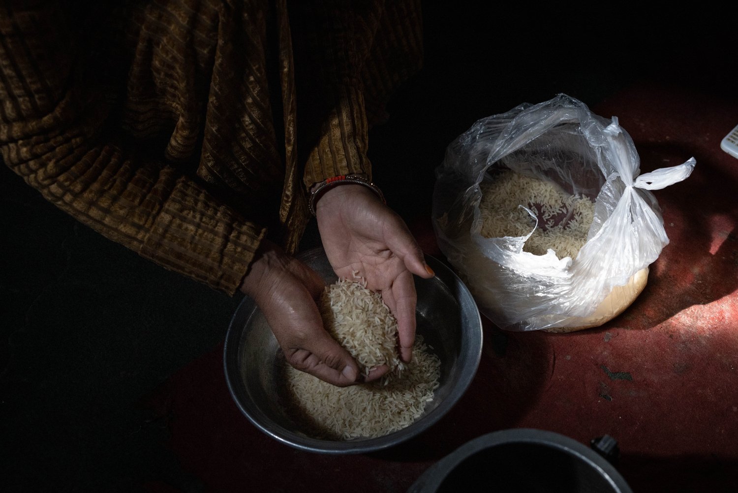 A woman's hands hold a handful of rice above a metal bowl.