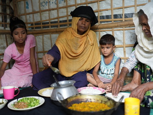Una madre y una abuela comen sentadas en el suelo de su alojamiento con dos niños pequeños.