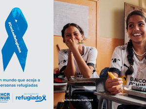 A la derecha, una foto de dos chicas jóvenes sonriendo y sentadas en sus pupitres en un aula. A la izquierda, un listón azul con la inscripción “Con los refugiados”. Debajo de la cinta se lee: “Por un mundo que acoja a las personas refugiadas”.