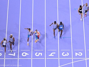 Vista aérea de cuatro parejas de corredores acercándose a la meta de una pista de atletismo de color morado con número y líneas blancas