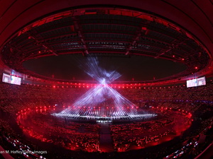 Rayos de luz blanca forman un cono gigante en el centro de un estadio a oscuras como parte de un espectáculo de luces