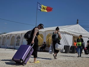 Personas cargadas de maletas caminan hacia una gran tienda de campaña sobre la que ondea la bandera de Moldavia