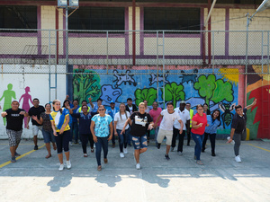 Un grupo de personas sonríe a la cámara en lo que parece una cancha de juego; detrás suyo, una pared muy colorida.