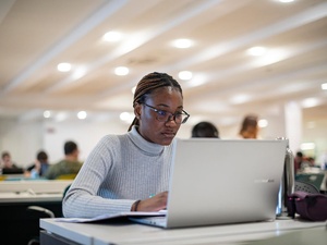 Una estudiante en su computadora portátil en una biblioteca universitaria